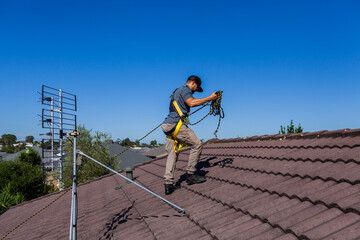 Tradie climbing on roof of house in safety harness to secure rope for safety compliance
