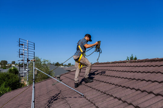 Tradie climbing on roof of house in safety harness to secure rope for safety compliance