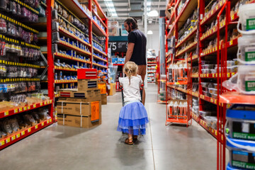 Toddler pushing tiny shopping trolley through hardware store following dad