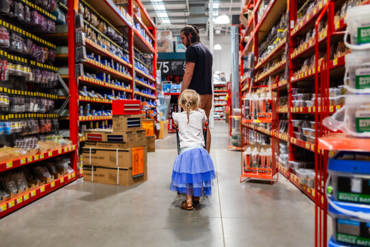 Toddler pushing tiny shopping trolley through hardware store following dad