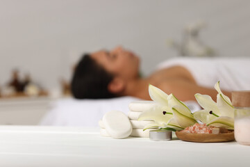 Beautiful woman relaxing on massage couch indoors, focus on different spa products and lily flowers