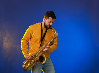 Fototapeta premium Professional musician playing saxophone on blue background