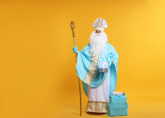 Saint Nicholas with Christmas gift and crozier on orange background, space for text