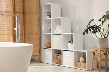 Stylish bathroom with shelving unit, bathtub and houseplants