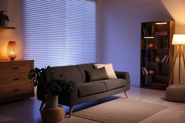 Stylish living room with comfortable sofa and wooden shelving unit in evening. Interior design