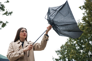 Woman with broken umbrella fighting wind outdoors, low angle view