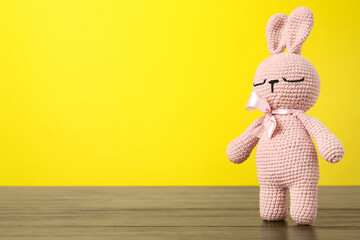Cute knitted toy bunny on wooden table against yellow background. Space for text