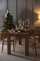 Christmas table setting with stylish dishware, glasses and burning candles in festive decorated room
