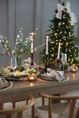 Christmas table setting with stylish dishware, glasses and burning candles in festive decorated room
