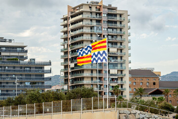 Badalona city flags fluttering in the wind, positioned in front of contemporary residential...