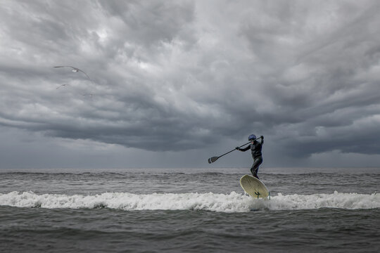 Paddleboarder navigating ocean waves under stormy sky with dramatic clouds