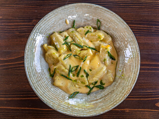 Plate of Potato Gnocchi in Creamy Cheese Sauce with Green Onion Garnish, Top View.Delicious Italian Gnocchi with Green Onions Served on a Textured Plate