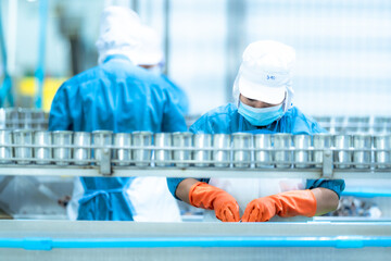 Worker wearing blue gloves sorting cans on a production line in a food processing factory. Hygiene,...