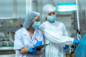 Female quality control inspectors wearing lab coats, masks, and hairnets examine a food sample in a...