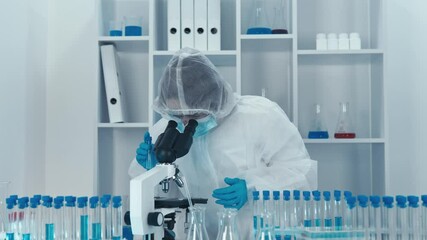 In a sterile lab, a dedicated scientist in protective gear examines test tubes and uses a microscope, showcasing advanced research techniques that lead to cuttingedge scientific discoveries