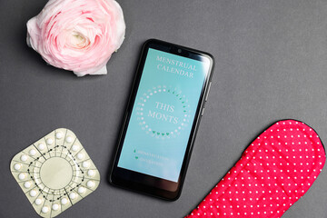 Smartphone with period calendar application, menstrual products and flower on grey background, flat...