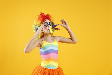Girl dressed like clown with blowers on yellow background. Surprise party