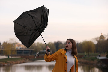 Teenage girl with broken umbrella fighting wind under rain outdoors