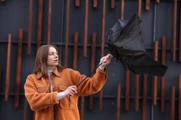 Teenage girl with broken umbrella fighting wind under rain outdoors