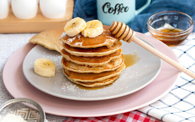 Pour maple syrup over homemade banana pancakes. A slide of hot pancakes with fresh bananas on a plate. Maple serop sprouts over pancakes. Portion of breakfast on a plate. High quality photo