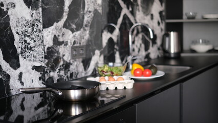 kitchen countertop with frying pan on stove and eggs with vegetables on table