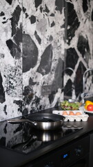 kitchen countertop with frying pan on stove and eggs with vegetables on table