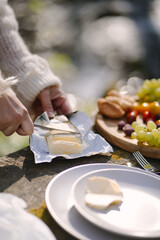 Young girl is cutting butter for the breakfast on the wooden table in the morning garden. Serving table with sandwiches and fruits in the nature