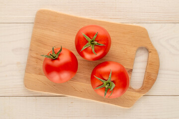 Red juicy tomatoes on a wooden kitchen board on a wooden table, close-up, top view.
