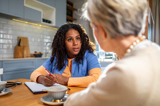 Home nurse talking with elderly woman at kitchen table