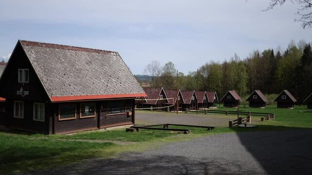 Quiet summer camp with rows of rustic wooden cabins stands empty under soft blue sky surrounded by green forest peaceful atmosphere perfect for outdoor adventures retreats and kids activities