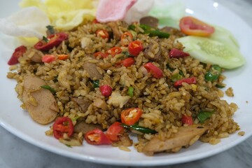 Close-up of spicy Indonesian fried rice (nasi goreng) garnished with sliced red chilies, vegetables, and crackers on a white plate