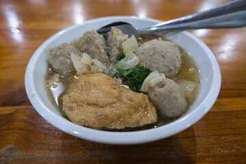 Close-up of a traditional Indonesian meatball soup or bakso served in a white bowl with tofu, vegetables, and savory broth