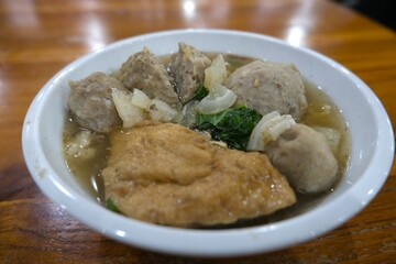 Close-up of a traditional Indonesian meatball soup or bakso served in a white bowl with tofu, vegetables, and savory broth