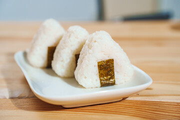 Onigiri made of rice and nori seaweed are spun on a white plate.
