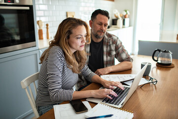 Couple reviewing household finances and bills on laptop in kitchen