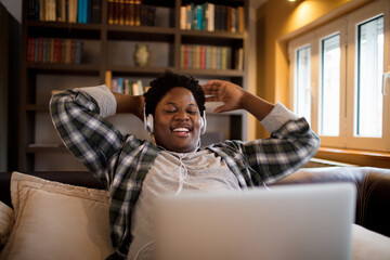Happy young man relaxing with headphones while watching laptop at home