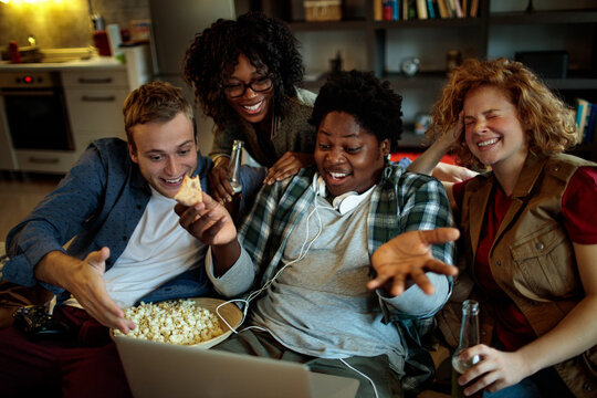 Group of friends drinking beer eating pizza and watching movie on laptop at home party