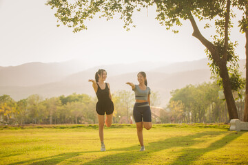 Two young Asian women exercising under a tree in the evening with beautiful golden sunlight. Healthy exercise concept. © ThawKyar