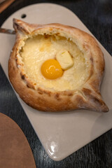 Delicious adjarian khachapuri with melted cheese and raw egg yolk on a plate