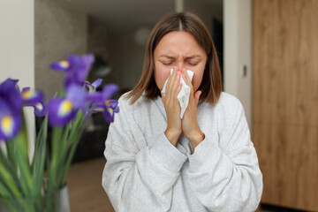 Seasonal allergy. Close up face of allergic young woman uses paper tissues from runny nose, sneezes...