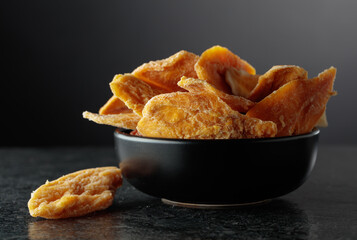Dried mango slices in a black dish on a black background.