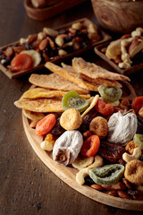 Mix of dried tropical fruits, nuts, and raisins on a wooden table.