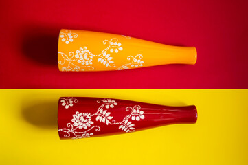 Dos elegantes jarrones de cerámica, uno amarillo y otro rojo, con intrincados diseños florales...