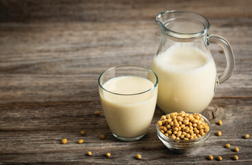 Soy milk in a glass and soybeans on the wooden table. Plant based vegetable milk, vegetarian,...