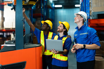 Diverse group of warehouse workers wearing reflective safety vests and helmets operating forklift...