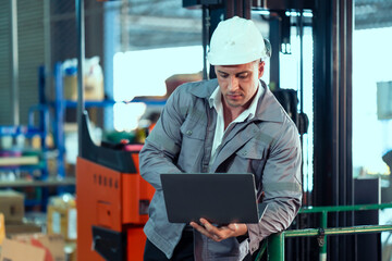 Warehouse male worker wearing helmet using laptop analyzing logistics data for warehouse management planning inventory control supply chain efficiency teamwork symbolizing industrial operation