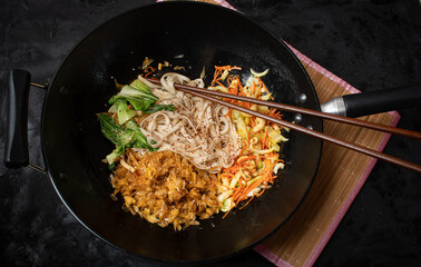 Vegan stir fry consisting of yuba, carrot, bok choy and noodles, served in wok
