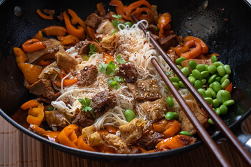 Vegan Stir Fry with yuba, seitan, bell pepper, edamame. .Wheat noodles, served in wok