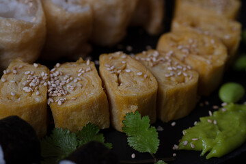 Vegan maki, inari sushi, tamagoyaki, edamame on black background