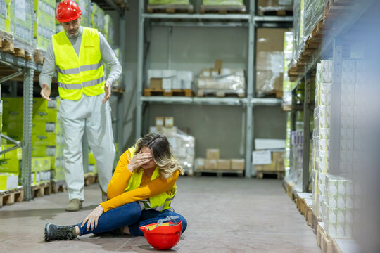 A warehouse worker comforts a colleague who has fallen, highlighting safety and teamwork in emergency situations.